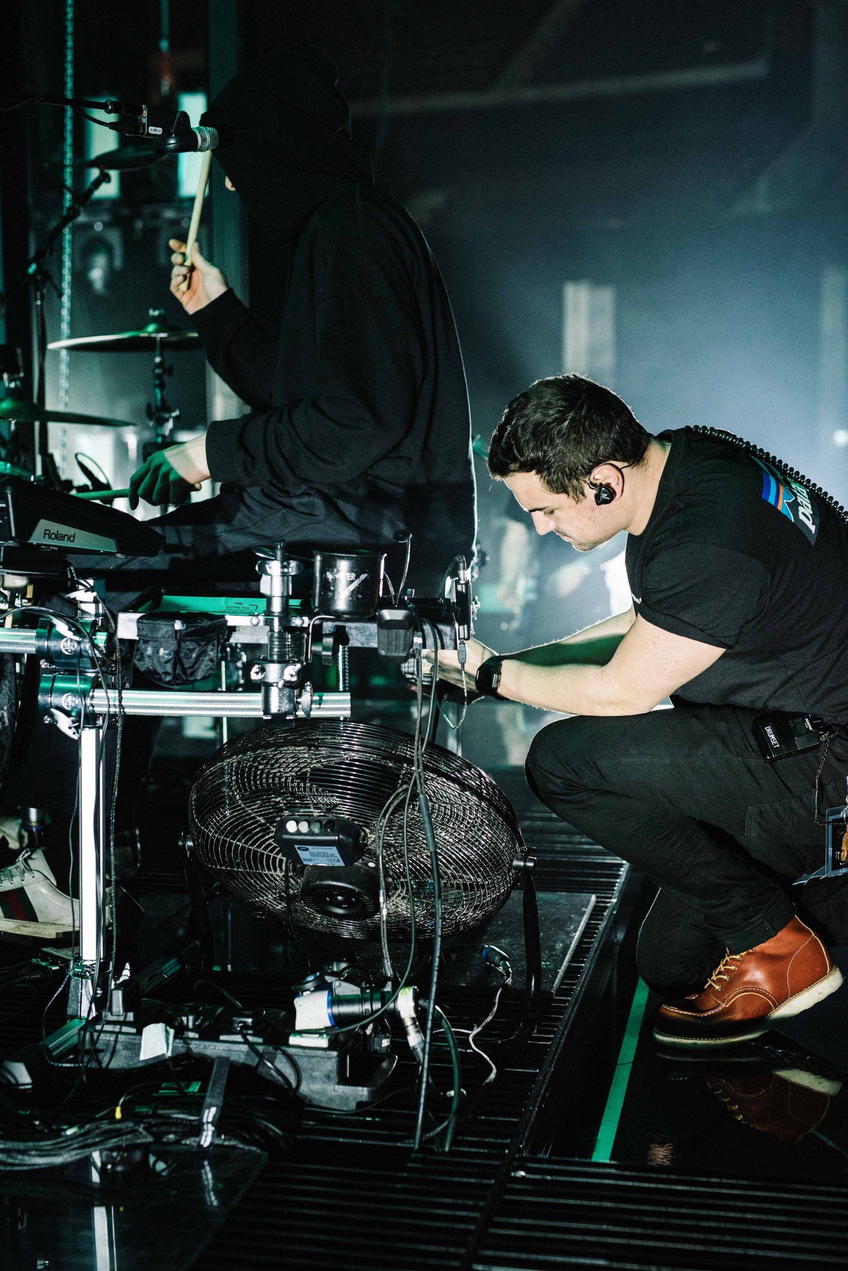 Drum tech Tom 'Woody' Wood assisting The 1975 drummer George Daniel